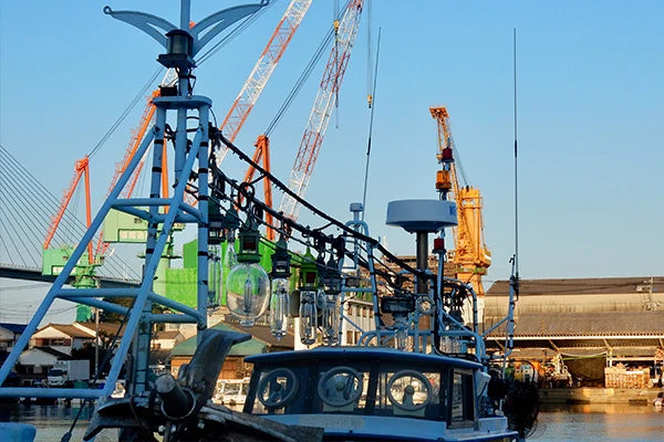 Boat in a harbor with cranes and buildings in the background