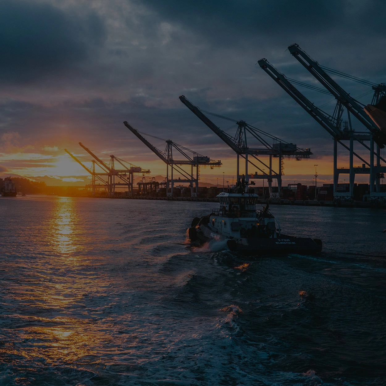 An oil rig near the ocean with a boat and sunset in the distance