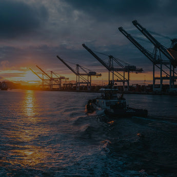 An oil rig near the ocean with a boat and sunset in the distance