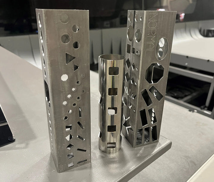 Three metal objects with geometric cutouts on a reflective surface
