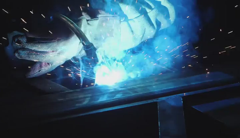 Employee welding stainless steel metal while wearing safety gloves with blue sparks flying out