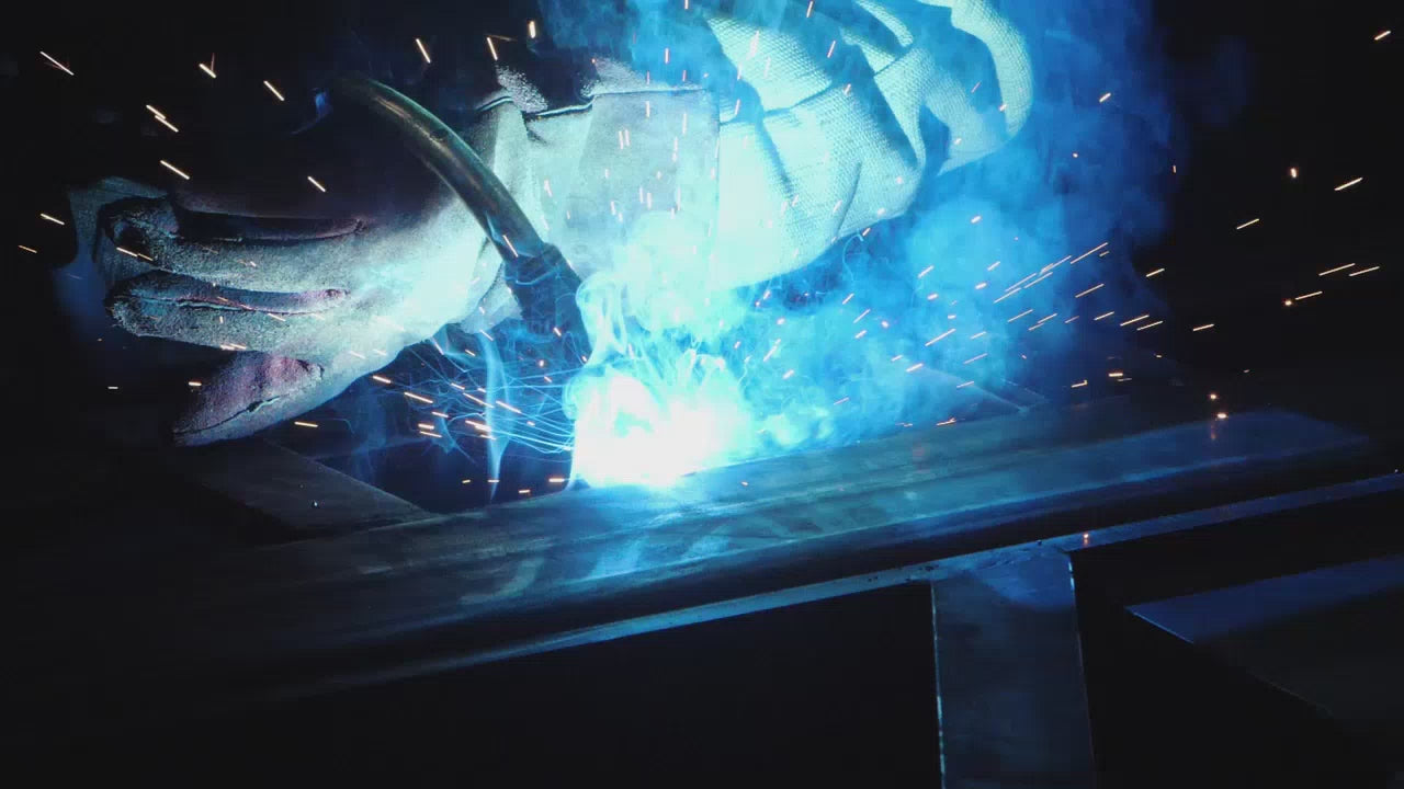 Employee welding stainless steel metal while wearing safety gloves with blue sparks flying out